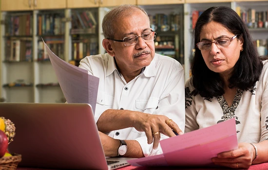 Two professionals reviewing documents together at a desk with a laptop, in a library setting with bookshelves in the background
