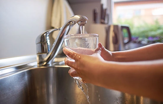 Child's hand filling a clear glass with tap water from a kitchen faucet over a sink